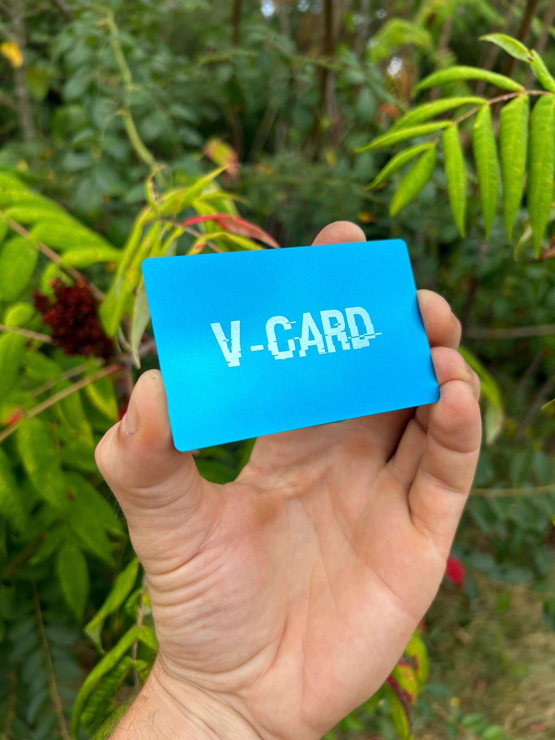 Hand holding a blue card with 'V-CARD' text against a green leafy background