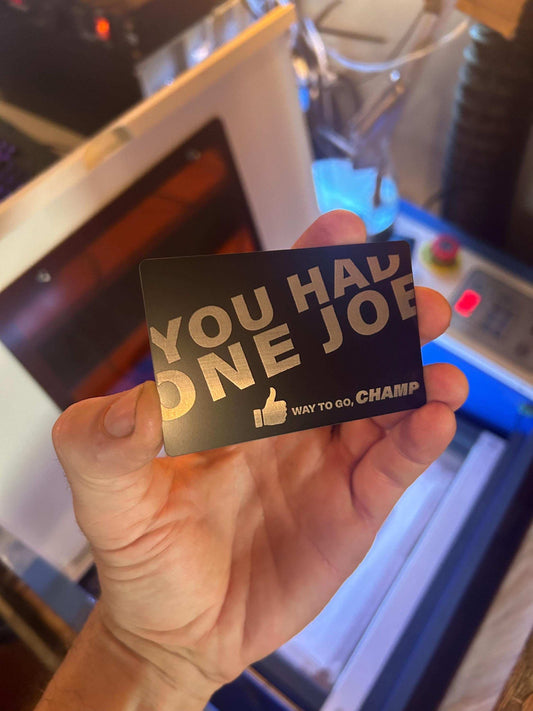 Hand holding a black card with silver Way To Go Champ text in an indoor setting