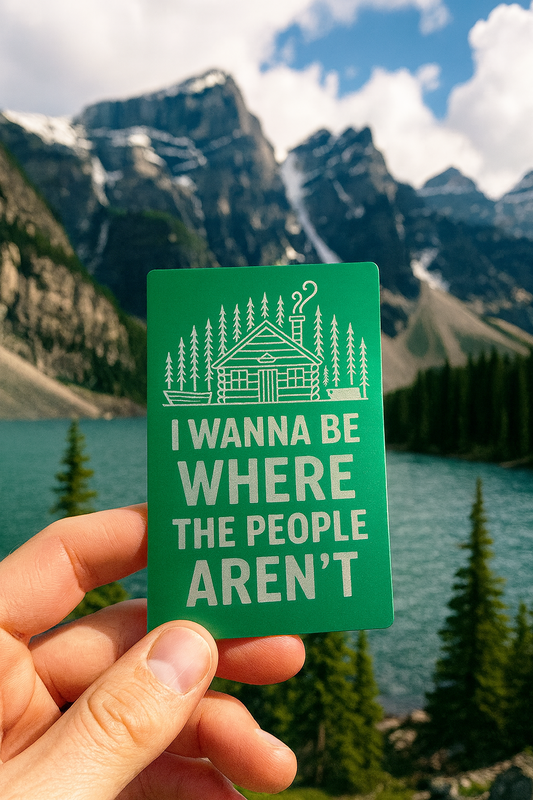Green metal placard with silver laser engraved text that reads: "I Wanna Be Where The People Aren't", held in front of a scenic mountain landscape
